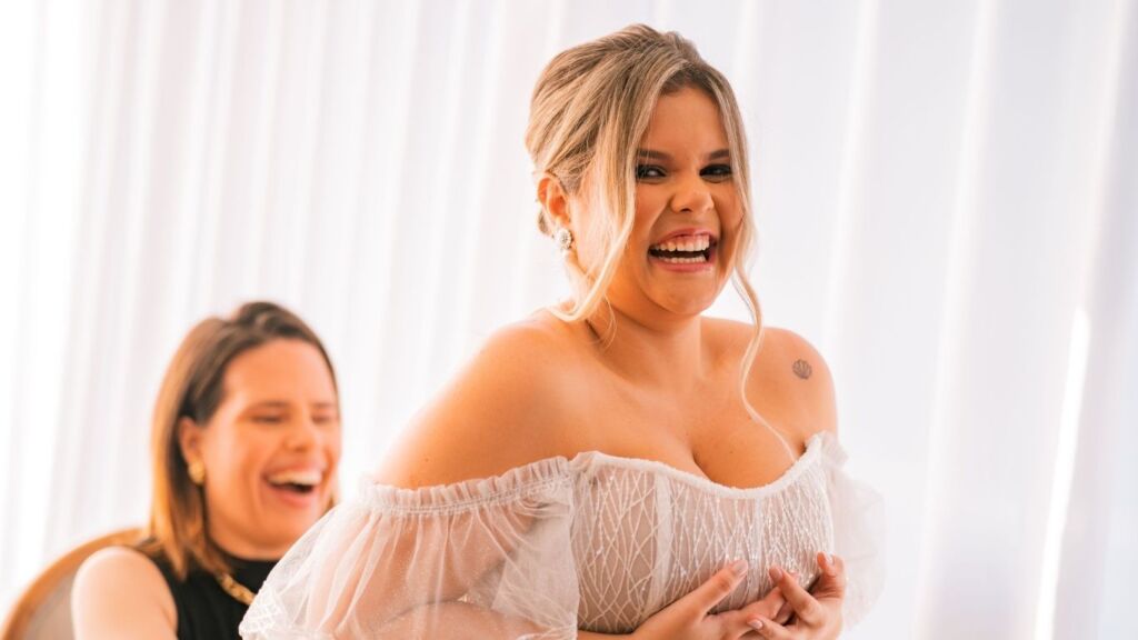 Noiva radiante e emocionada com penteado romântico e maquiagem natural personalizada por visagismo, demonstrando autenticidade e felicidade genuína durante preparativos do casamento com Mariana Botelho